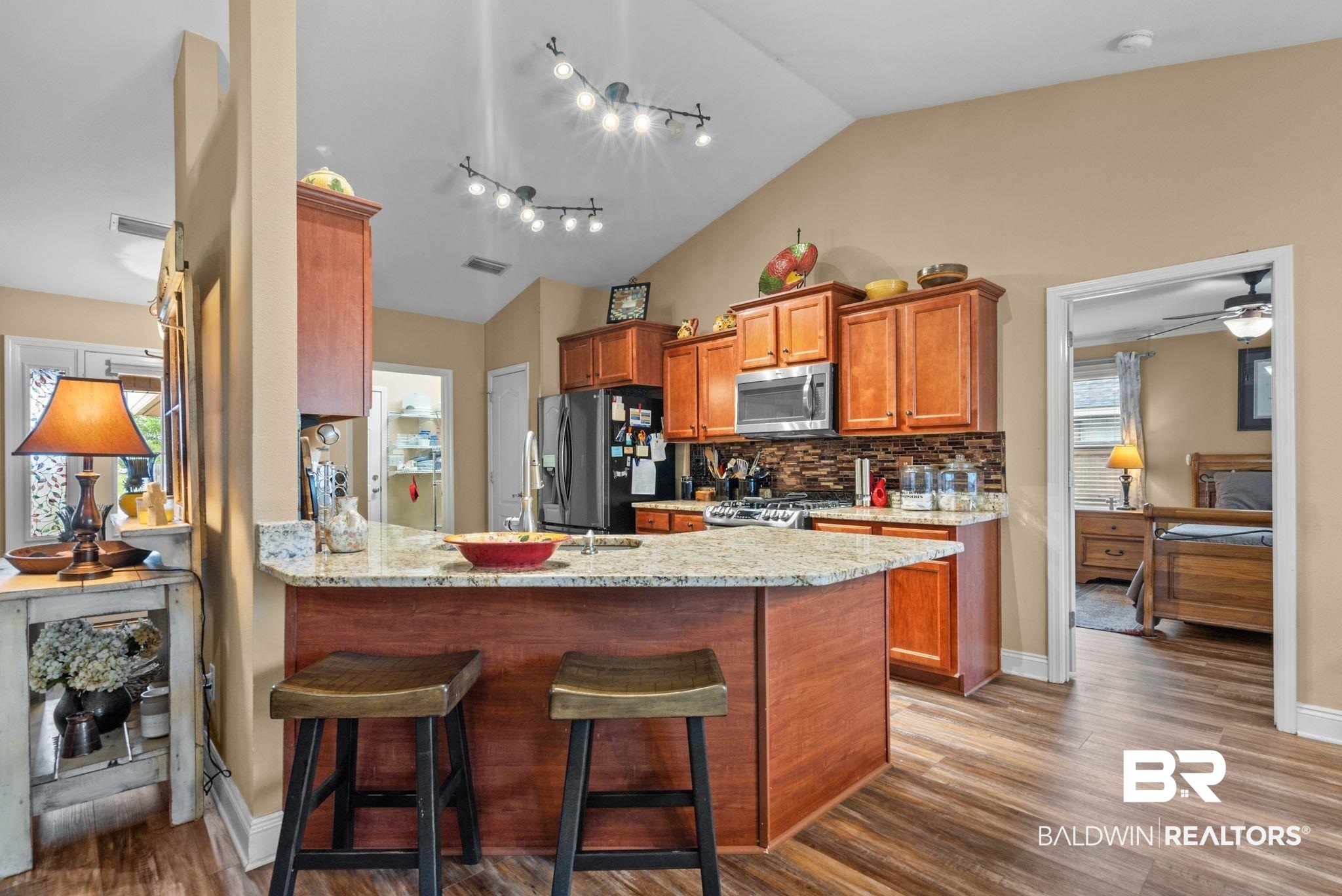 562 Vestige Mews Foley, AL 36535 - Photo 16 of 54 Kitchen featuring wood-finish flooring, a vaulted ceiling, wood cabinetry, stainless steel appliances, and an island with a stone-finish countertop