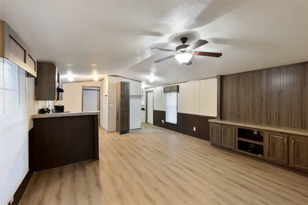 a living room with stainless steel appliances kitchen island granite countertop a refrigerator a stove a microwave oven with white cabinets and wooden floor