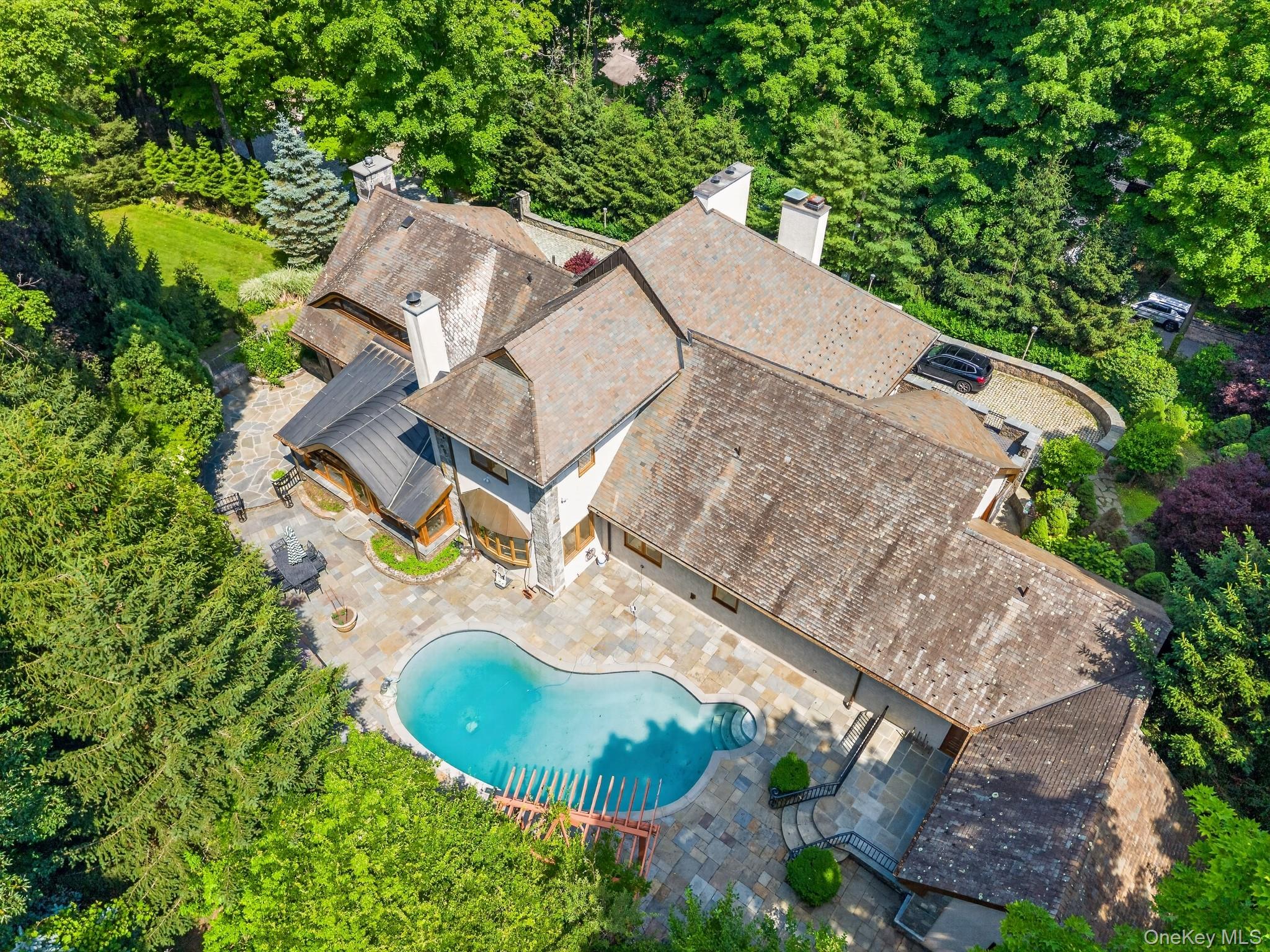 23 Inningwood Road Ossining, NY 10562 - Photo 3 of 50 Large property featuring a freeform swimming pool with integrated spa, extensive stone patio surround, and multiple gabled rooflines
