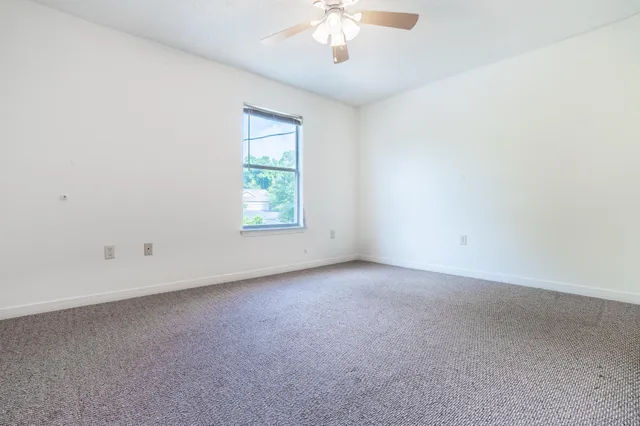 an empty room with a chandelier fan and windows
