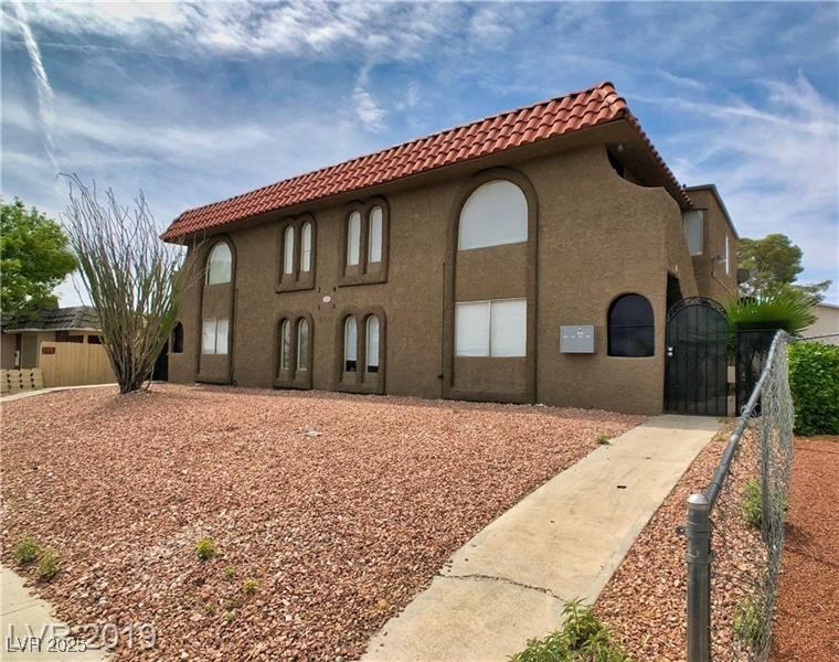 View of side of property featuring a tile roof, stucco siding, and a gate