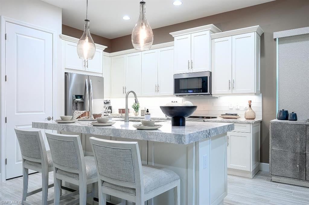 7164 Cayo Coco Lane Naples, FL 34113 - Photo 9 of 17 a kitchen with stainless steel appliances granite countertop a stove top oven a sink a dining table and chairs with wooden floor