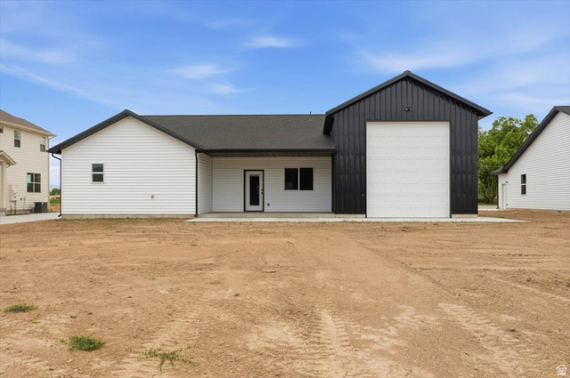 164 North 400 East Preston, ID 83263 - Photo 19 of 21 Rear exterior featuring a black metal-clad workshop addition with a large white roll-up door, white vinyl siding, a dark shingle roof, and a concrete patio space