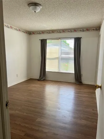 an empty room with wooden floor and windows with curtains