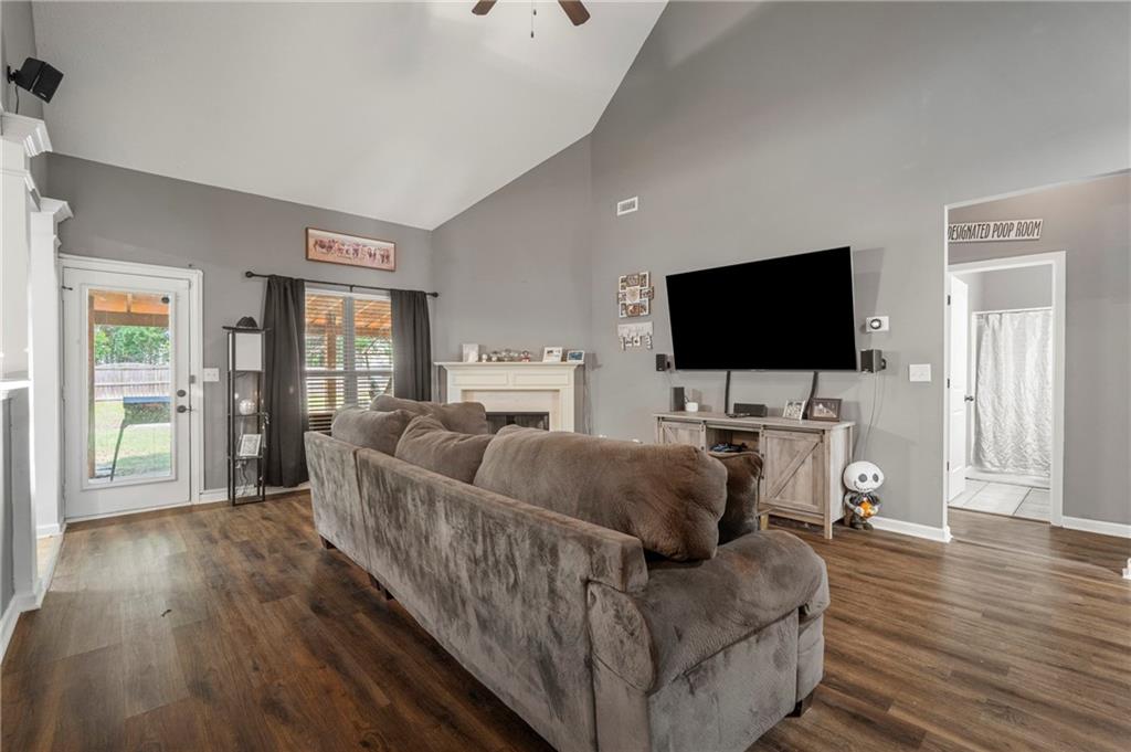 Living area featuring high vaulted ceiling, a ceiling fan, a fireplace, dark wood-style floors, and baseboards