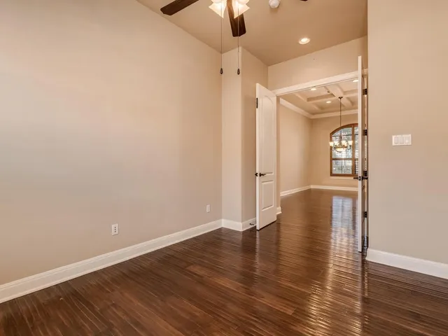 a view of an empty room with wooden floor and a ceiling fan