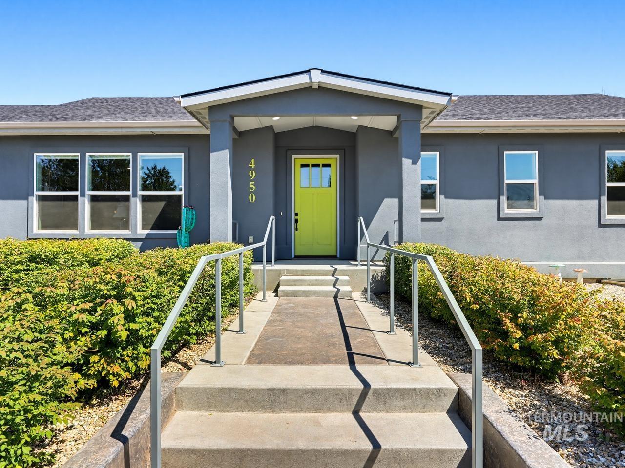 4950 West Columbia Road Nampa, ID 83687 - Photo 5 of 50 Contemporary exterior featuring a bright green entry door, covered porch, multiple windows, and a paved walkway with handrails