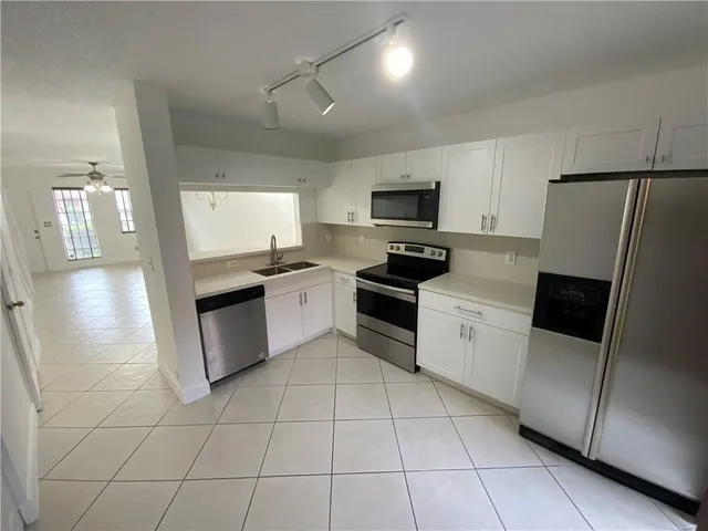 a kitchen with granite countertop a refrigerator sink and white cabinets