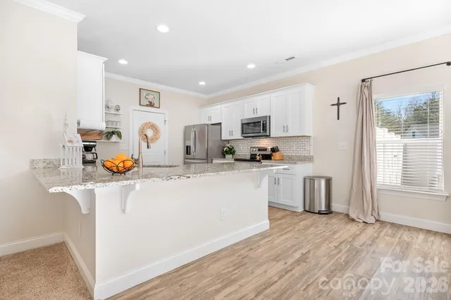 a kitchen with stainless steel appliances granite countertop a stove a sink a refrigerator and white cabinets with wooden floor