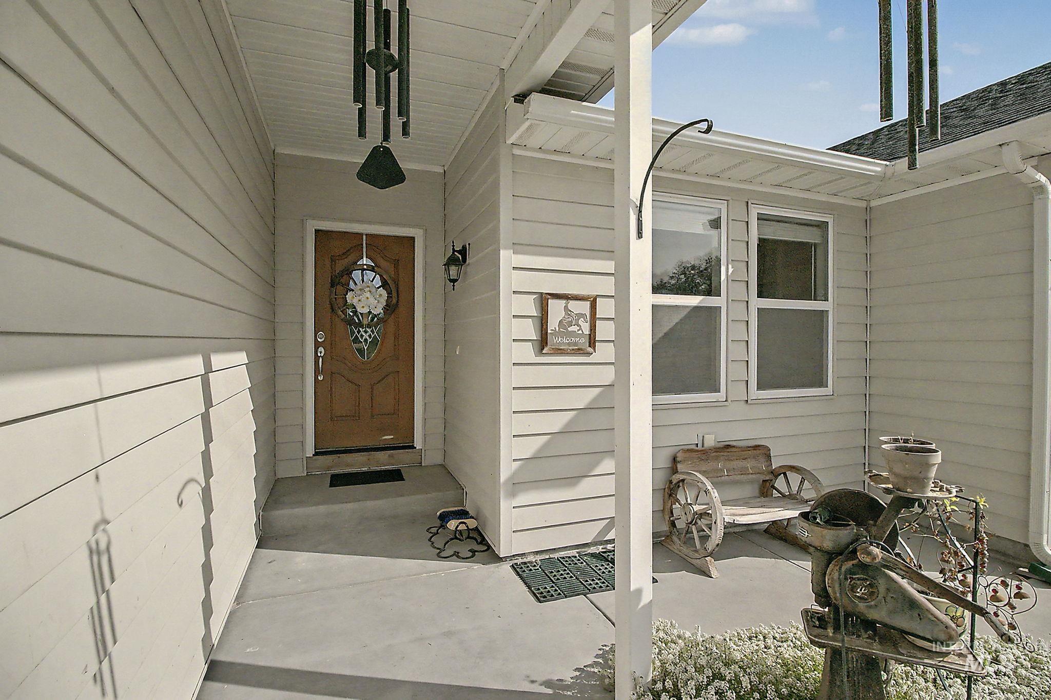 6900 West Charters Lane Melba, ID 83641 - Photo 7 of 49 Covered front porch featuring a wood-panel entry door with decorative glass, side wall sconce, and two windows with white trim