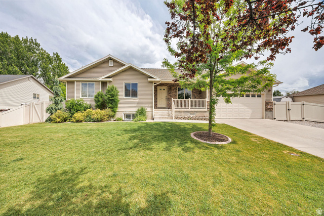 2912 South 1080th Street West Logan, UT 84321 - Photo 2 of 43 Ranch-style exterior with stone and siding accents, featuring a two-car garage, front porch with white railing, established landscaping, and a concrete driveway