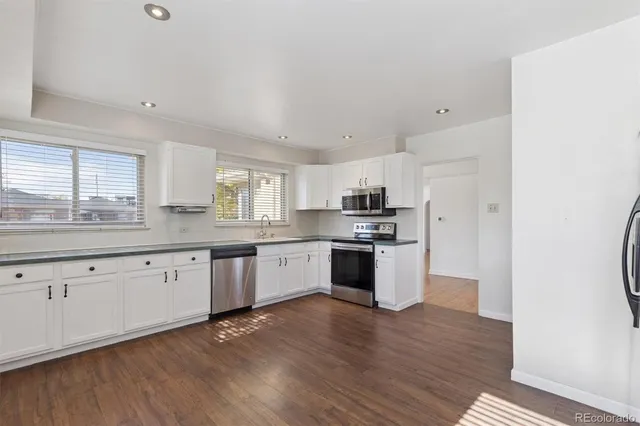 a large kitchen with stainless steel appliances granite countertop a stove a sink dishwasher and a refrigerator with wooden floor