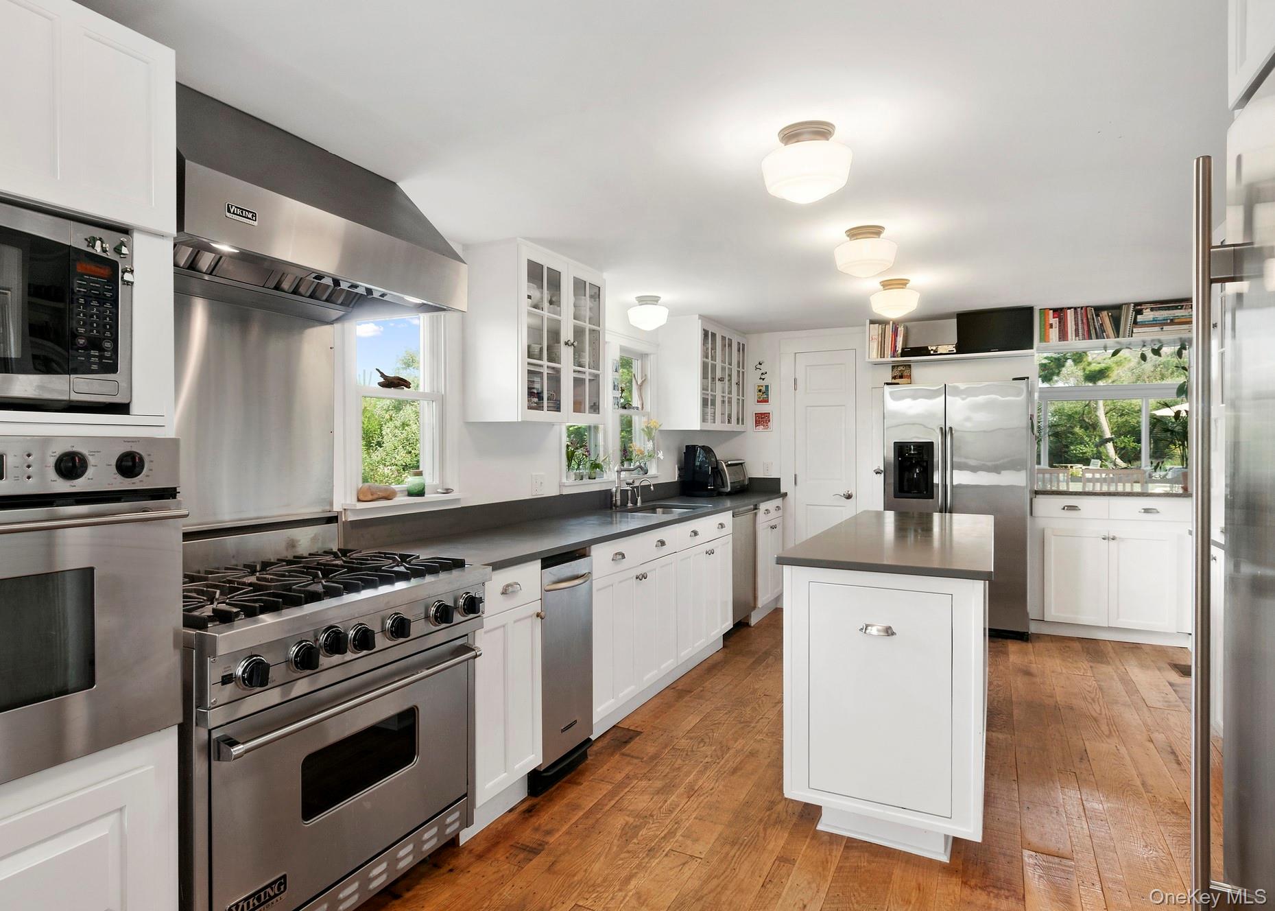 162 Dune Road Quogue, NY 11959 - Photo 11 of 28 a kitchen with stainless steel appliances white cabinets a sink a stove a refrigerator and island with wooden floor