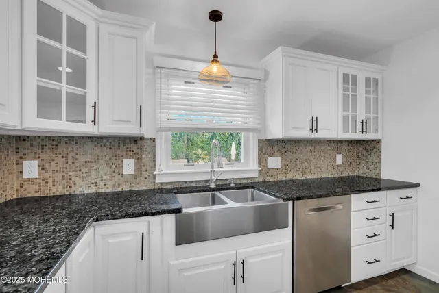 a kitchen with granite countertop a sink white cabinets and a window