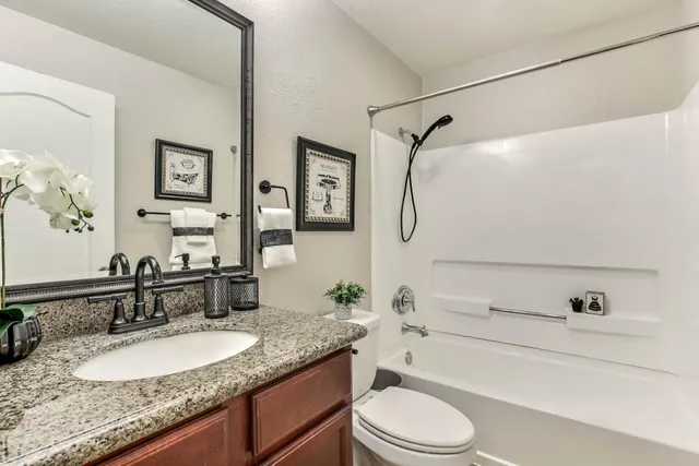 a bathroom with a granite countertop sink vanity mirror bathtub shower and a toilet