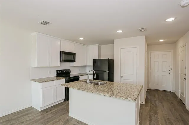 a kitchen with granite countertop a refrigerator stove a sink and white cabinets with wooden floor