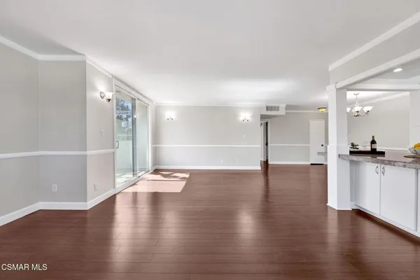 a view of an empty room with wooden floor and a kitchen