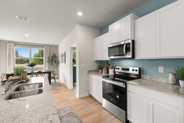 a kitchen with stainless steel appliances granite countertop a refrigerator a sink a stove a dining table and chairs with wooden floor