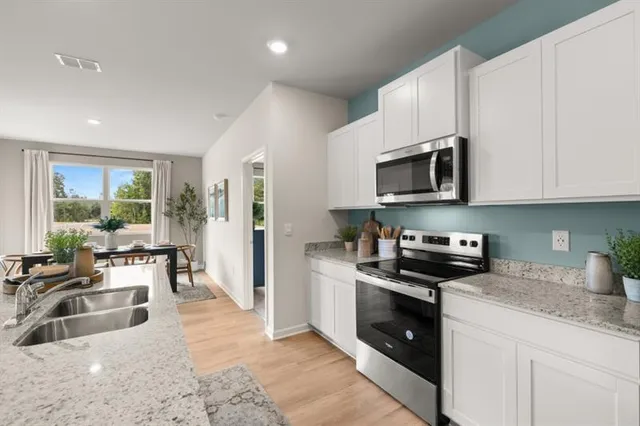 a kitchen with stainless steel appliances granite countertop a refrigerator a sink a stove a dining table and chairs with wooden floor