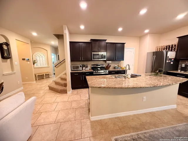 a large kitchen with kitchen island granite countertop a stove a sink a counter top space and cabinets