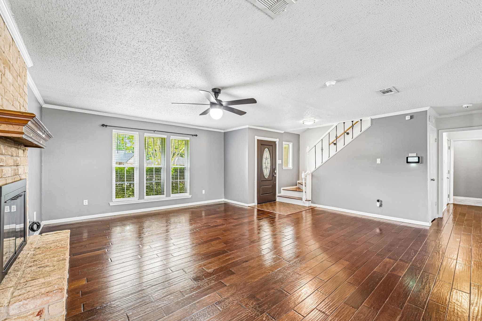 8 Arlington Street Conroe, TX 77301 - Photo 13 of 37 This spacious living room features elegant hardwood floors, a cozy fireplace, and abundant natural light from large windows. The modern ceiling fan, neutral wall colors, and open layout create a welcoming atmosphere, while a staircase leads to the upper level.