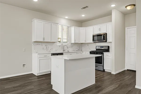 a kitchen with stainless steel appliances granite countertop a stove top oven a sink a refrigerator and white cabinets with wooden floor