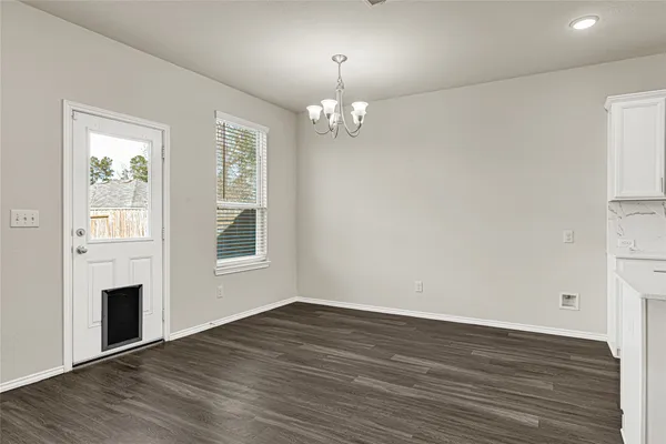 an empty room with wooden floor chandelier and windows
