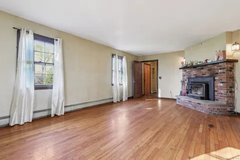 an empty room with wooden floor fireplace and windows