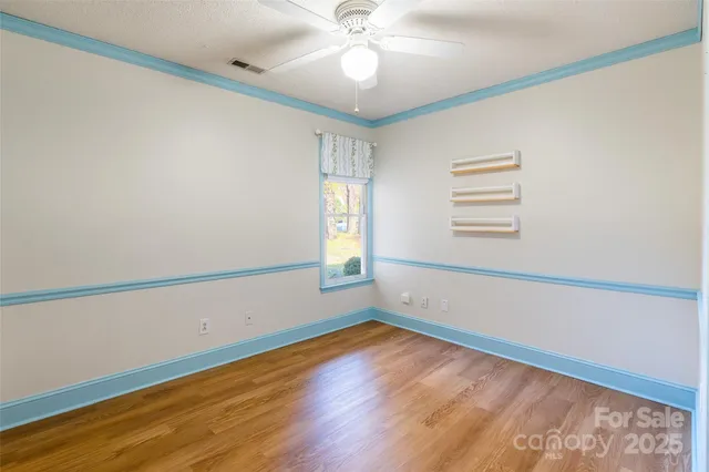 a view of empty room with wooden floor and fan