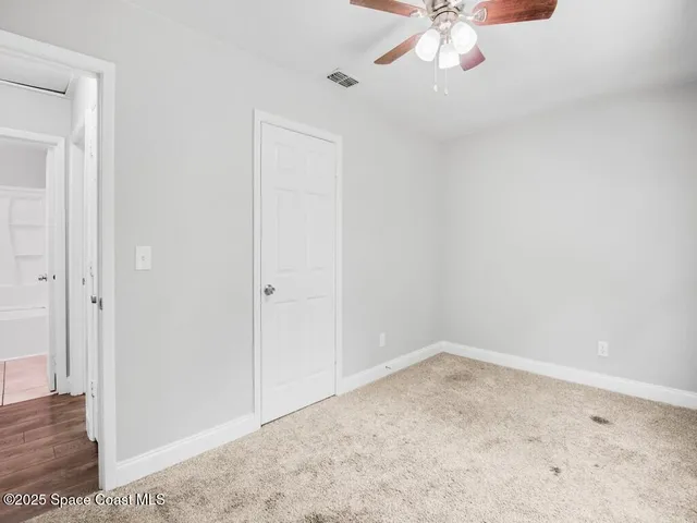 an empty room with a chandelier fan and wooden floor