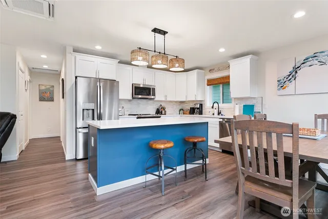 a kitchen with stainless steel appliances granite countertop a refrigerator a stove top oven a sink dishwasher and a dining table with wooden floor