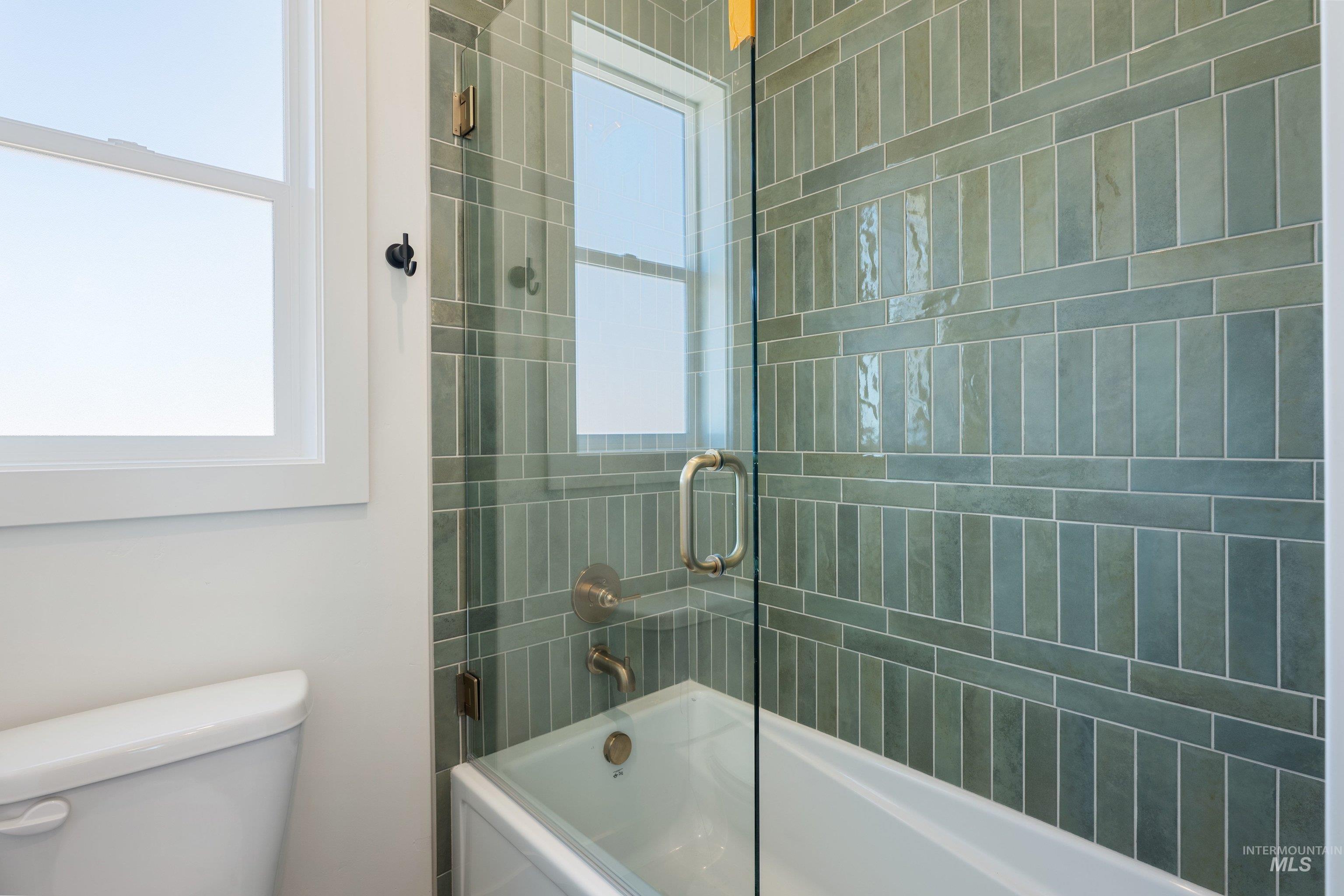24821 Ardmore Court Caldwell, ID 83607 - Photo 33 of 43 Bathtub and shower combination featuring floor-to-ceiling green subway tile with horizontal accent bands, a clear glass shower enclosure, brushed nickel fixtures, and a white framed window
