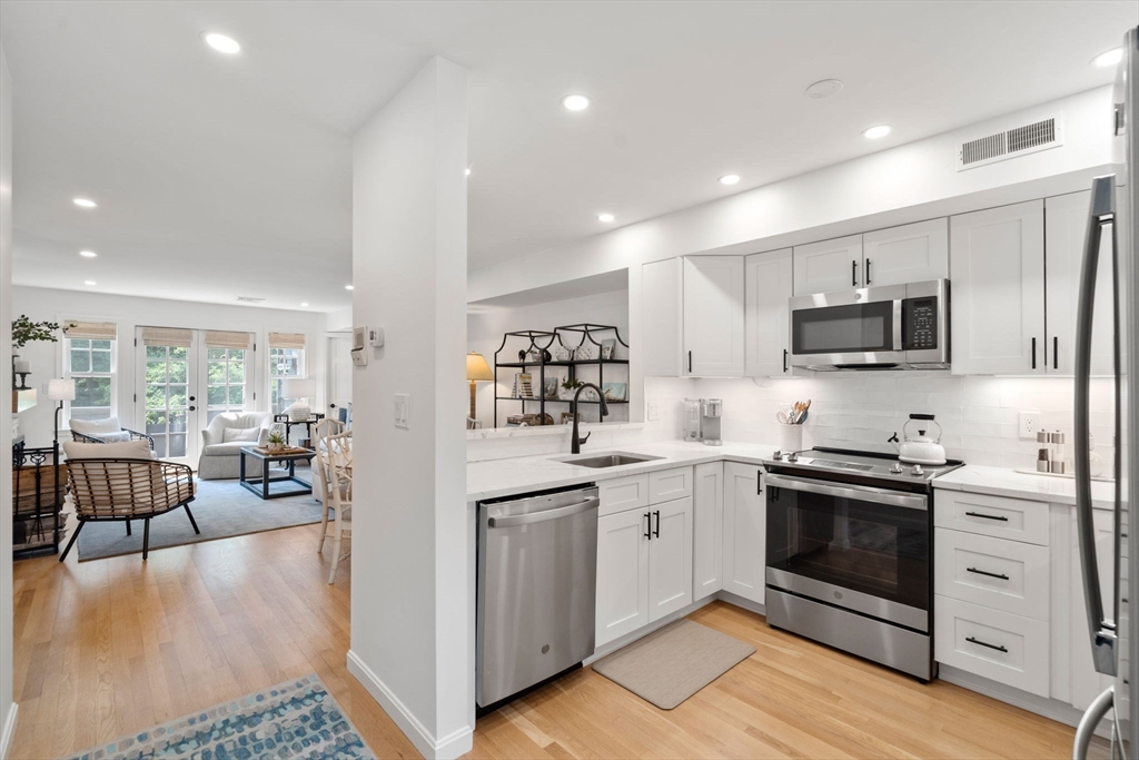 27 R West Street, Unit 13 Beverly, MA 01915 - Photo 3 of 34 a kitchen with stainless steel appliances granite countertop a stove top oven a sink dishwasher a dining table and chairs with wooden floor