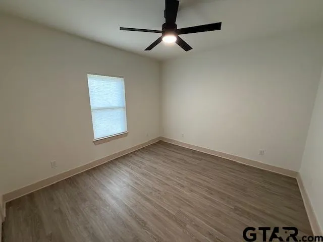 an empty room with wooden floor ceiling fan and windows