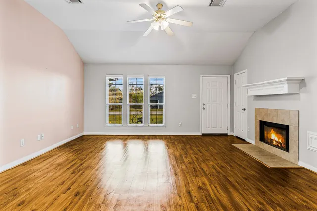 a view of an empty room with wooden floor fireplace and a window