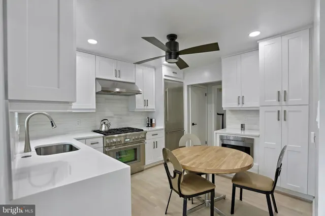 a kitchen with stainless steel appliances a stove a sink a refrigerator a stove a refrigerator with white cabinets and wooden floor