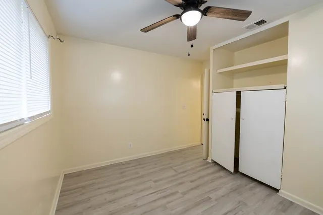 an empty room with wooden floor closet and windows