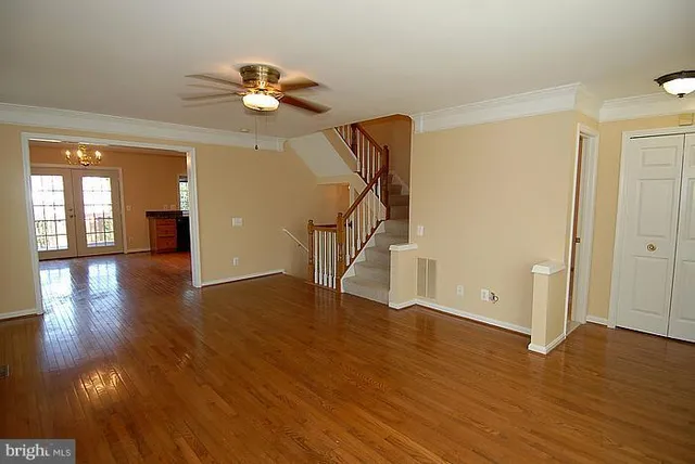 a view of an empty room with wooden floor and a ceiling fan