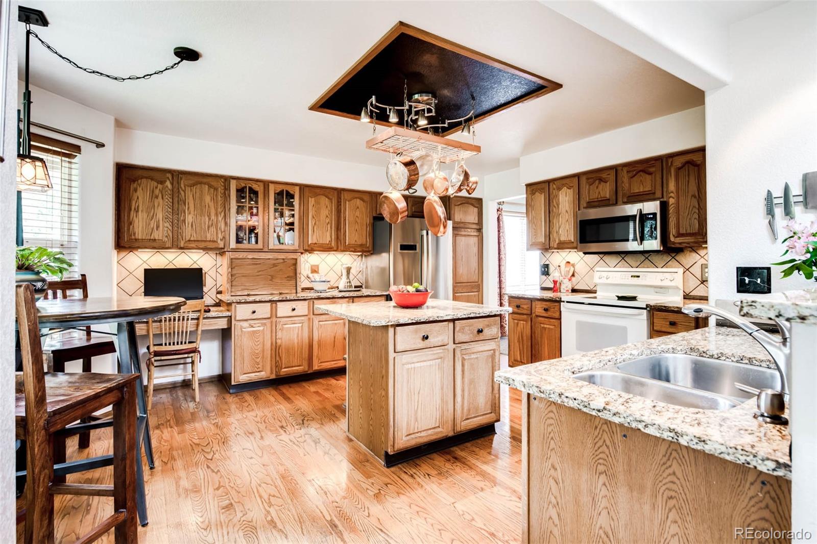 6549 Poppy Street Arvada, CO 80007 - Photo 5 of 33 a kitchen with stainless steel appliances kitchen island granite countertop a stove top oven a sink a dining table and chairs with wooden floor