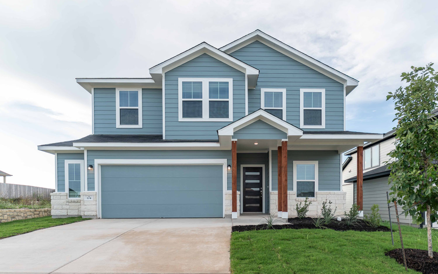View of front of home with a garage, concrete driveway, stone siding, a front yard, and covered porch