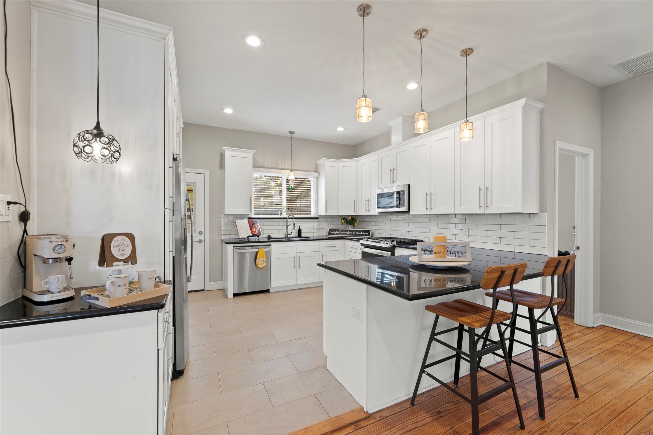 711 4th Street Sealy, TX 77474 - Photo 12 of 37 Elegant kitchen features a modern design with white cabinetry, stainless steel appliances, and a stylish subway tile backsplash. It has a central island with seating, pendant lighting, and ample counter space, offering both functionality and elegance.