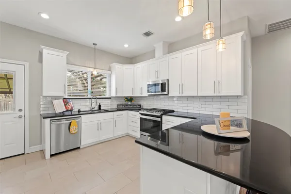 a kitchen with granite countertop a sink stove a refrigerator and white cabinets with wooden floor