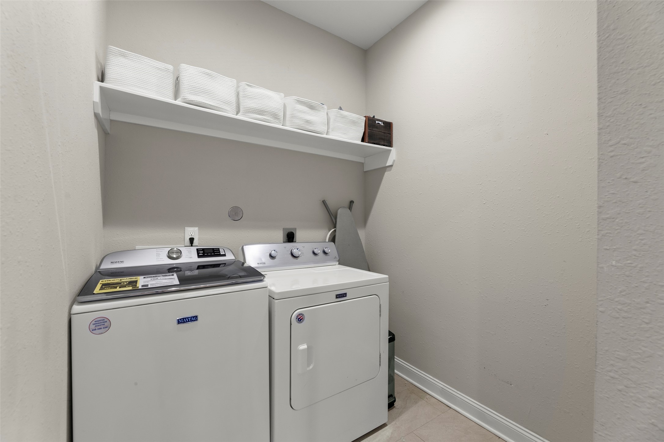 711 4th Street Sealy, TX 77474 - Photo 30 of 37 Compact laundry room with a washing machine and dryer. Shelving above provides storage for essentials, and the neutral walls create a clean, tidy space.