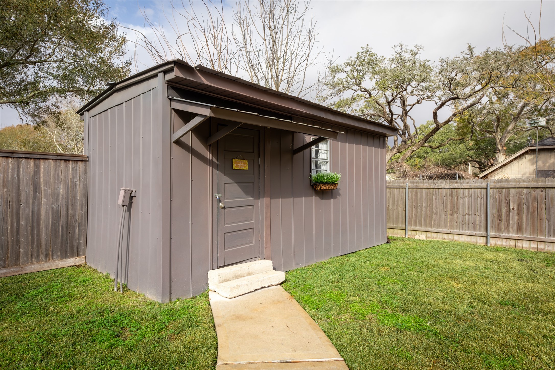 711 4th Street Sealy, TX 77474 - Photo 31 of 37 Spacious backyard detached flex space with a single door and window, nestled in a fenced yard with green grass and surrounded by trees. Perfect for storage or a small workspace.