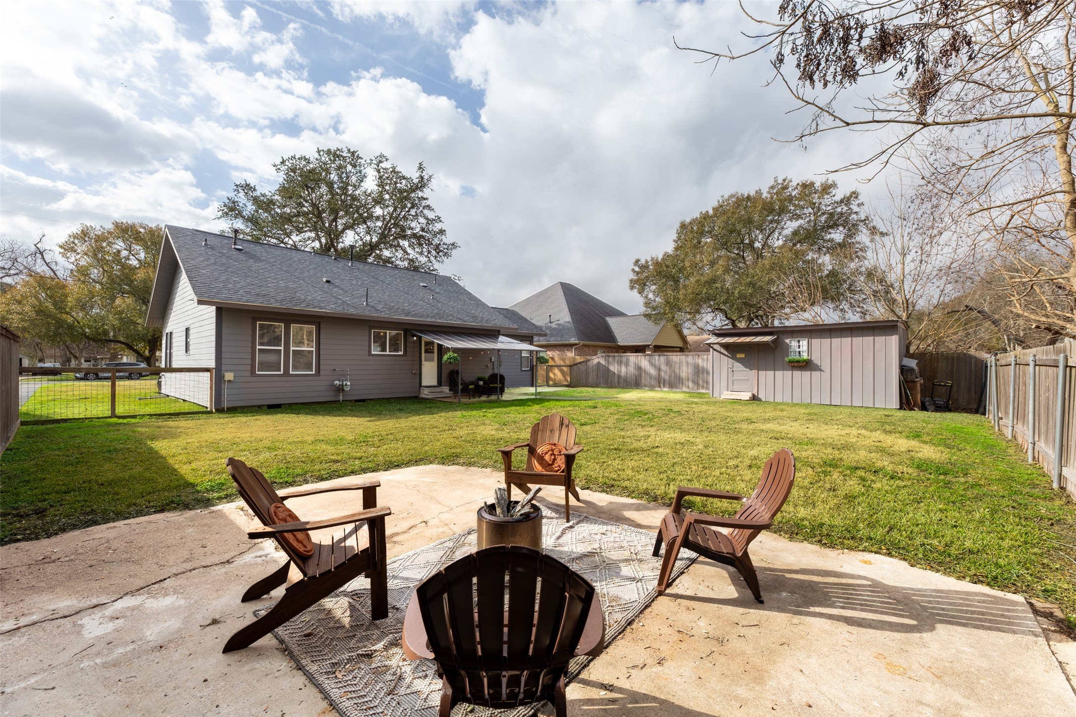 711 4th Street Sealy, TX 77474 - Photo 34 of 37 Spacious backyard with a patio featuring relaxed seating around a fire pit. Well-maintained lawn, a storage shed, and a fenced perimeter offer privacy and functionality. Ideal for outdoor gatherings and relaxation.