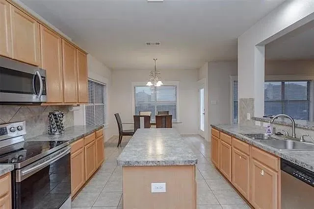 a large kitchen with granite countertop a sink dishwasher a stove top oven a refrigerator with wooden cabinets and floor