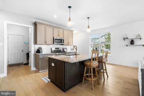 a kitchen with stainless steel appliances granite countertop a stove top oven a refrigerator a sink and a dining table with wooden floor