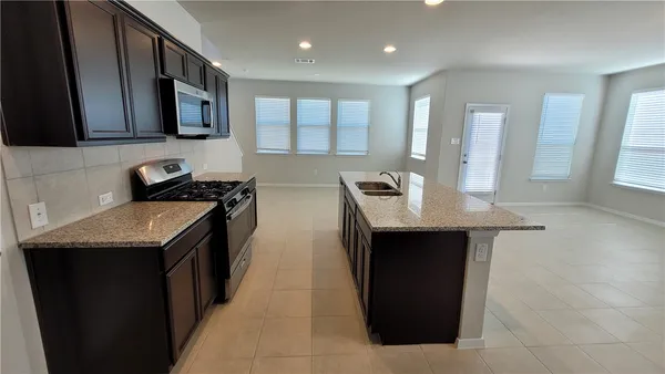 a kitchen with granite countertop a sink a stove top oven and wooden cabinets