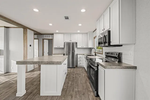a kitchen with stainless steel appliances granite countertop a stove top oven a sink and white cabinets