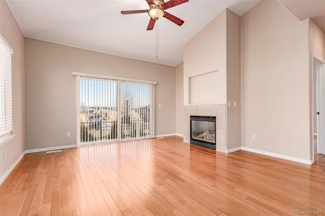 an empty room with windows a fireplace a ceiling fan and wooden floor